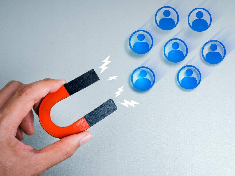 uma mão segurando um ímã puxando pessoas, simbolizando como conseguir leads qualificados